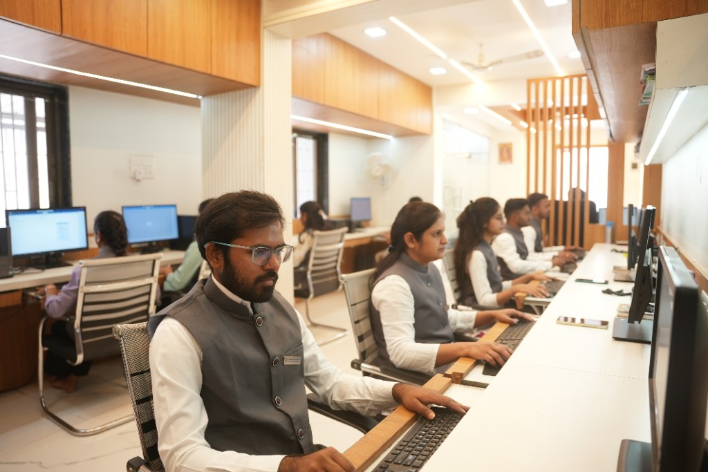 Professional team working at desks in a modern, well-lit office with white workstations and wood cabinetry